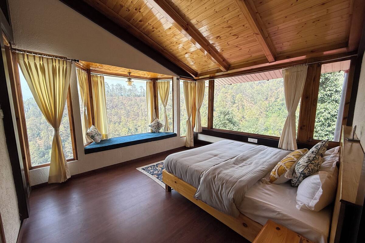 Une chambre avec un lit en bois, un coin fenêtre agrémenté de rideaux et une vue sur une zone boisée.