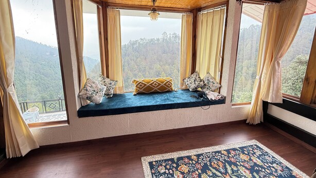 Une pièce dotée d’une banquette intégrée donnant sur un paysage montagneux, d’un plancher en bois et d’un tapis à motifs.