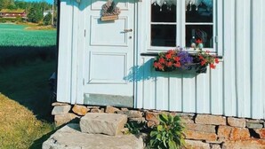 A white wooden building with a stone foundation, a door with a 'Welcome' sign, and a window with a flower box.