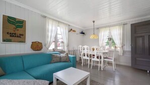A cozy living room with a teal sofa, white coffee table, and a dining area with white chairs and a small table.