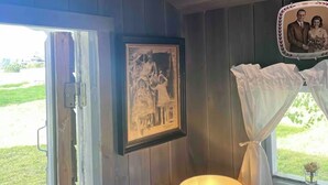 A room with wooden walls, a framed photograph, a lamp, and a window with curtains.