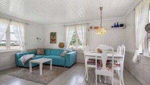 A room with a blue sofa, white dining table, and chairs, a small white table, and a hanging light fixture.