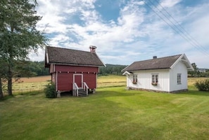 A red barn and a white house with a sloped roof, surrounded by a grassy field and trees.