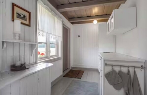 Una habitación estrecha con techo de madera, una ventana con cortinas, un lavamanos pequeño y un perchero para toallas.