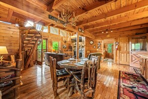 Een rustiek houten interieur met een eethoek, inclusief een houten tafel, stoelen, een trap en een kroonluchter.