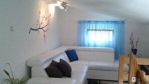 En moderne stue med en hvid sofa, et lille bord med en plante og en træstol.