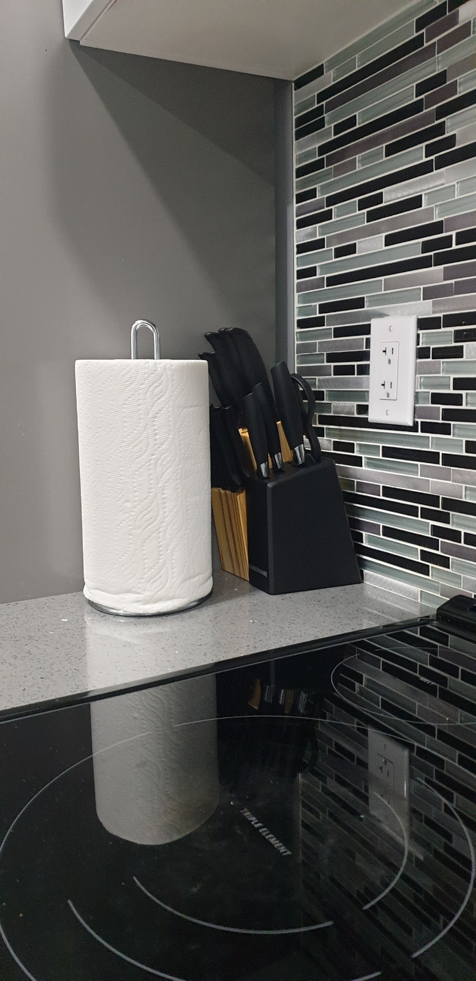 A kitchen counter with a paper towel holder, a knife block, and a backsplash with a mosaic tile pattern.