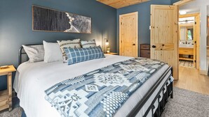 A bedroom with a bed, a wooden ceiling, a wall-mounted artwork, and a wooden door leading to a bathroom. - Ski-In/Out Luxury•1 Blk to Main•Pool+Hot Tub•Sauna (Breckenridge)