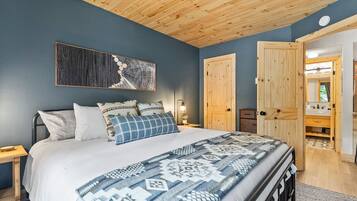 Une chambre à coucher avec un lit, un plafond en bois, une œuvre d’art accrochée au mur et une porte en bois donnant accès à une salle de bain.