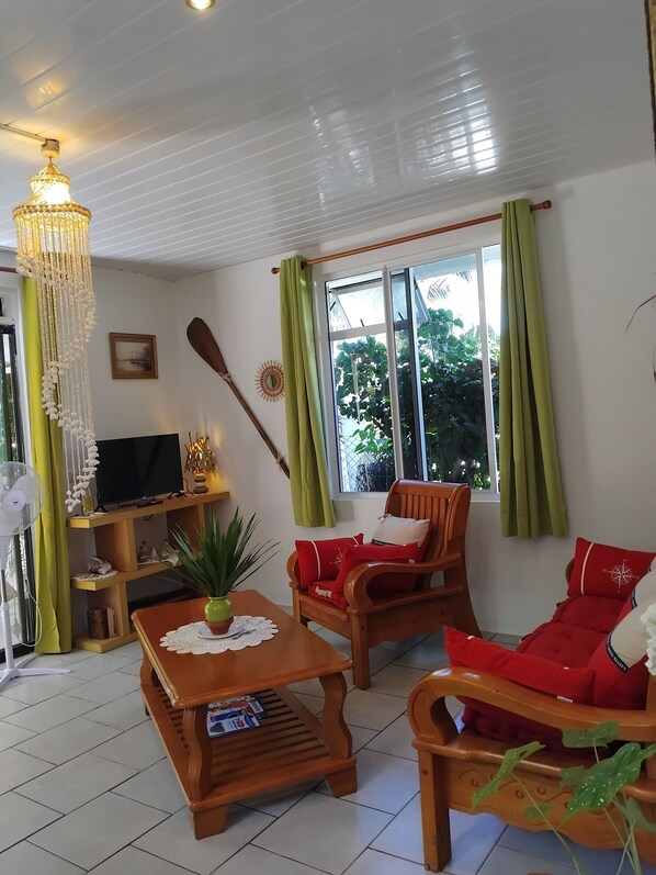 A living room with a television, wooden furniture, a fan, and a window with curtains.