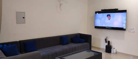 A modern living room with a sectional sofa, a glass-top coffee table, and a mounted TV.