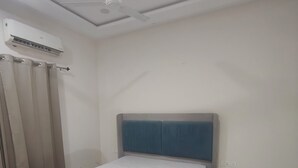 Een slaapkamer met een bed, een plafondventilator, een airconditioning en een gordijn.
