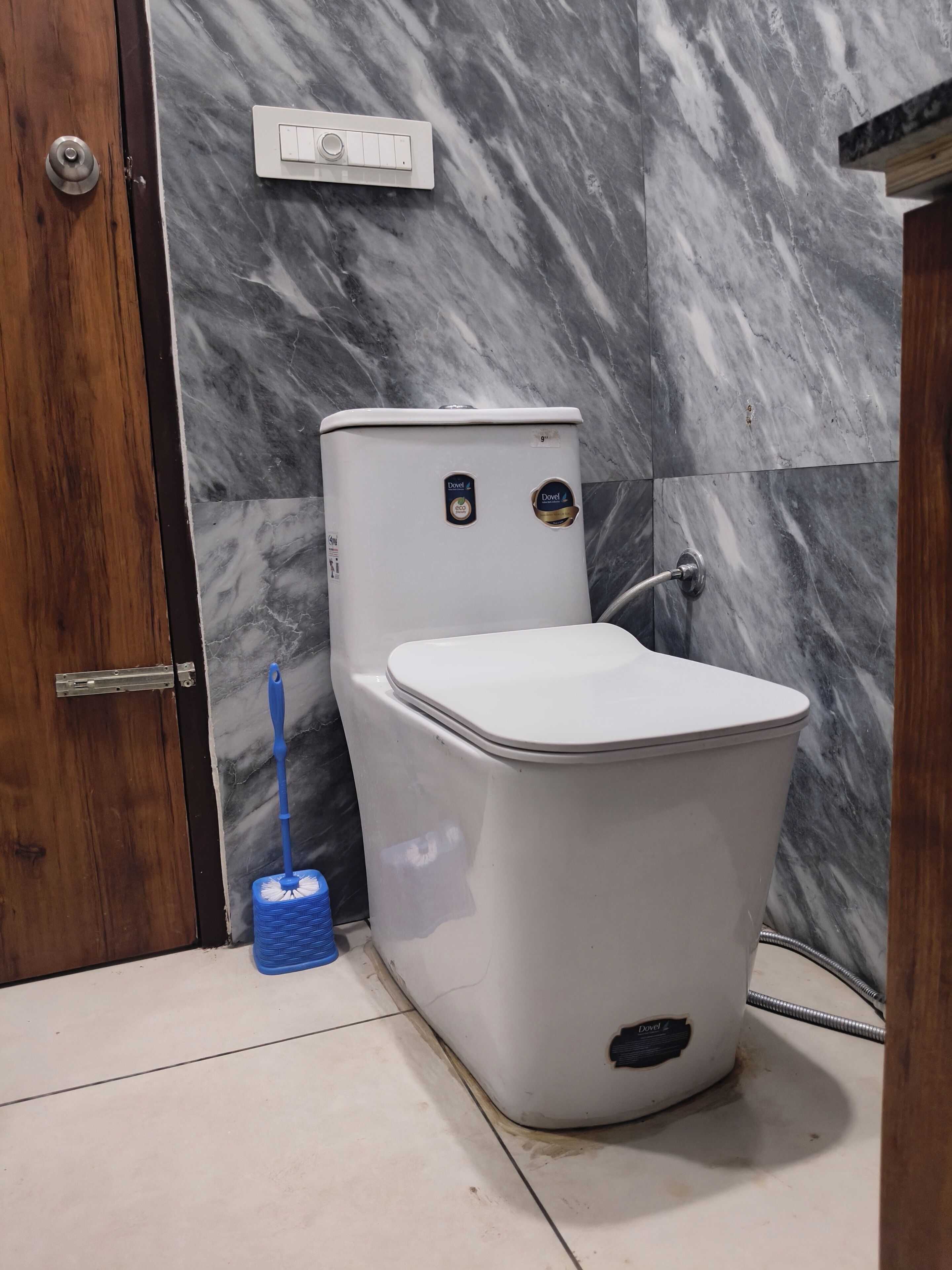 Un baño con un inodoro blanco, un escobillón de vaso azul y una pared de mármol.