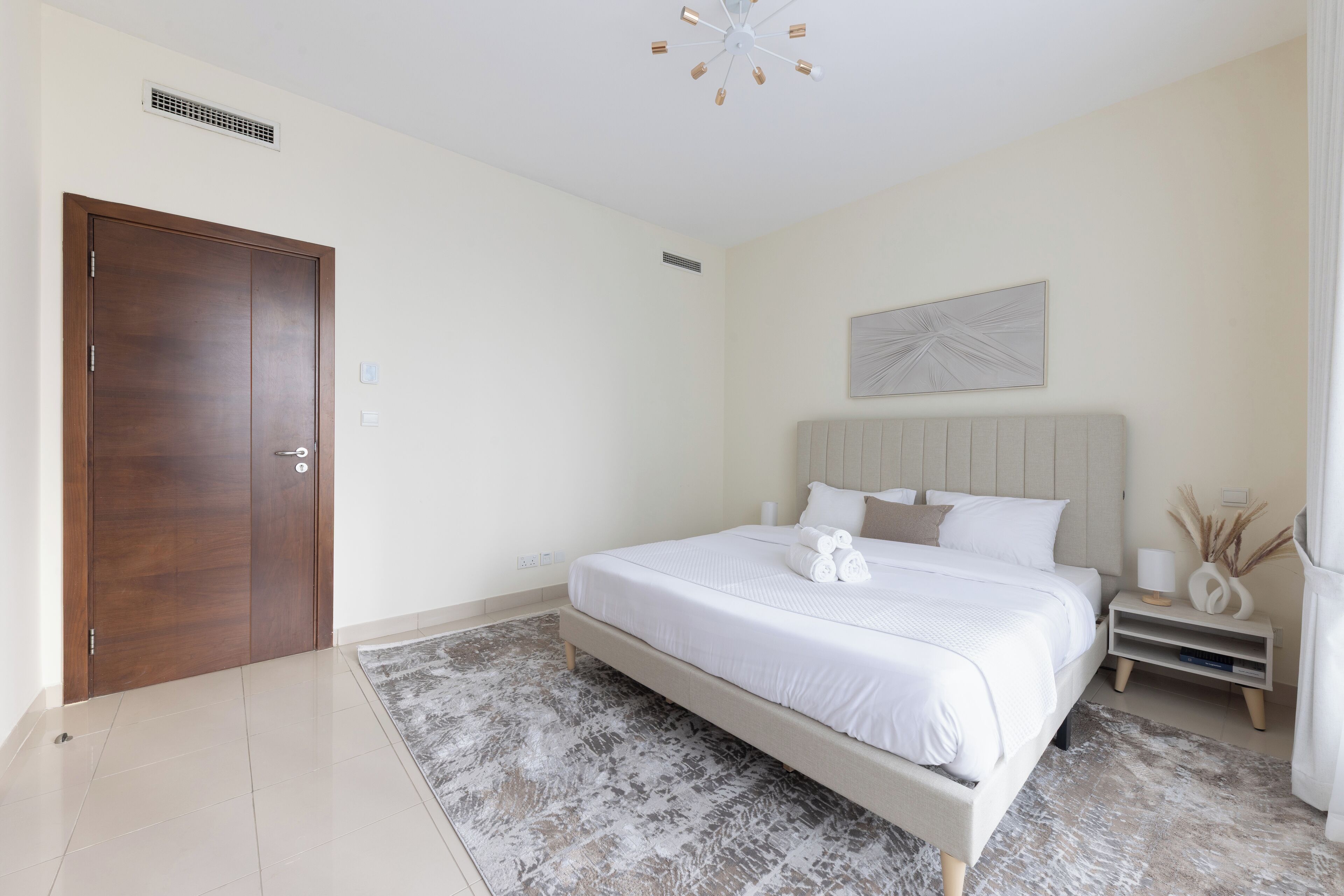 Un dormitorio con una cama grande, una puerta de madera, una lámpara en el techo y una obra de arte colgada en la pared.