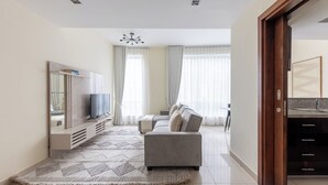 Una sala de estar moderna con un sofá gris, un televisor de pantalla plana y un espejo grande. Hay una alfombra estampada en el suelo y una lámpara en el techo.