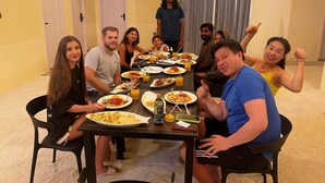 A group of people seated around a table with food and drinks, in a room with doors and a television on the wall. - Alsha Inn Dhiffushi (Dhiffushi)