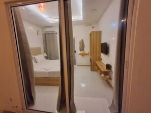 A hotel room with a bed, a mirror, a TV, and a wooden shelf.