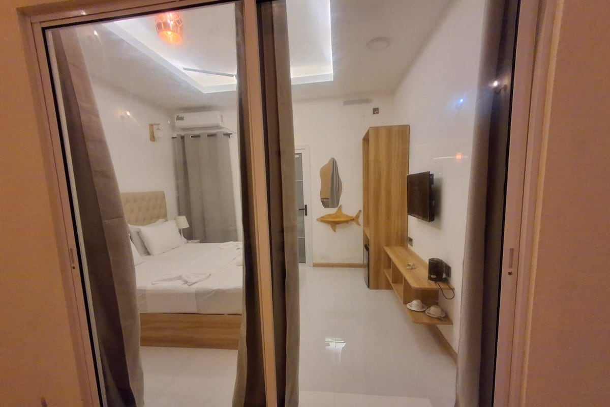 A hotel room with a bed, a mirror, a TV, and a wooden shelf.