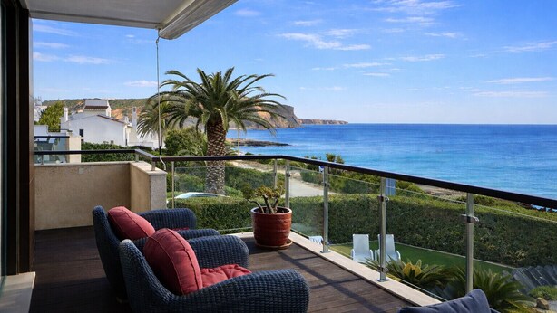 A balcony with wicker furniture and a potted plant, overlooking a coastal landscape with a clear view of the sea and distant buildings. - Luz by Check-in Portugal (Lagos)