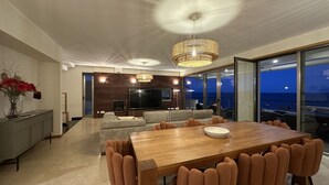 A modern living room with a wooden dining table, comfortable seating, a large TV, and a view of the ocean through large windows. - Luz by Check-in Portugal (Lagos)