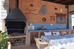 An outdoor kitchen with a brick oven, a sink, and a table set for dining. - Idyllic Andalusian villa with private pool & stunning views (Riogordo)