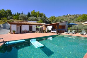 A swimming pool with lounge chairs and a small building with a tiled roof.