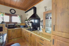 A kitchen with wooden cabinets, a stove, a microwave, and a clock on the wall. - Idyllic Andalusian villa with private pool & stunning views (Riogordo)