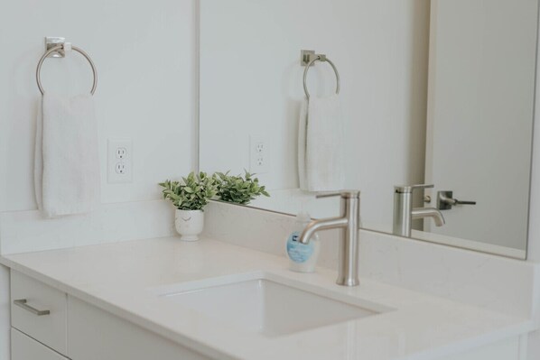 Une salle de bain avec un lavabo blanc, deux porte-serviettes, une plante en pot et un miroir.