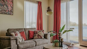 A living room with a sofa, a round coffee table, and a view of a lake through large windows. - Westergeest beneden 2 slaapk (Uitgeest)