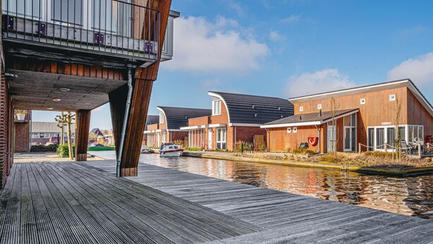 A waterfront property with modern wooden buildings, a covered walkway, and a canal. - Westergeest beneden 2 slaapk (Uitgeest)