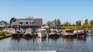 A marina with various boats docked, a modern building with large windows, and a clear blue sky. - Westergeest beneden 2 slaapk (Uitgeest)