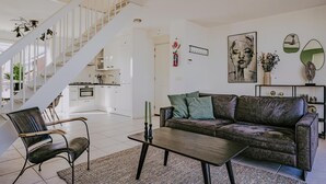 Ein modernes Wohnzimmer mit einer Couch, einem Couchtisch und einem Sessel. Eine Treppe führt zu einer oberen Ebene.