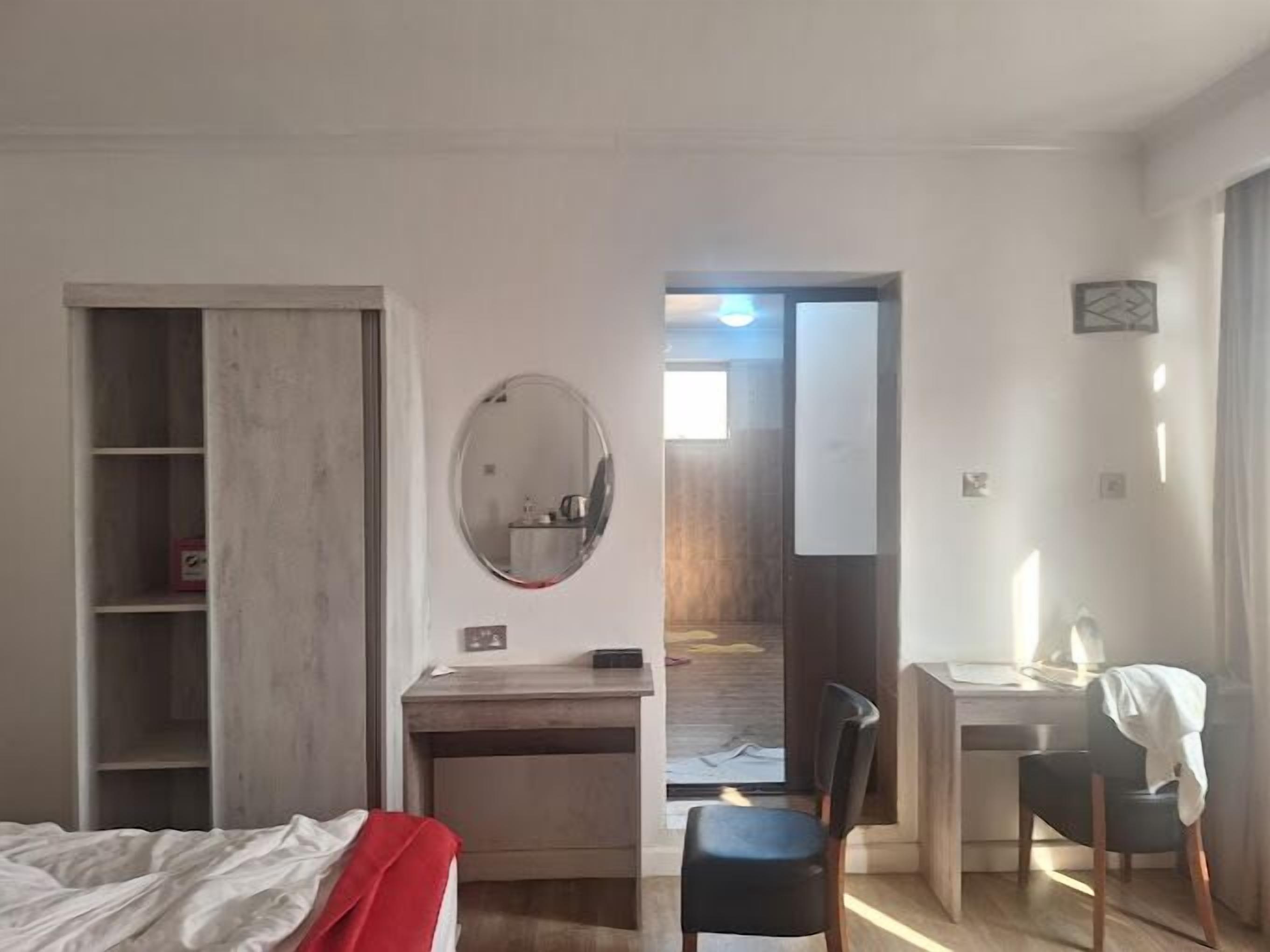 A hotel room with a bed, a desk, a chair, a mirror, and a wardrobe.