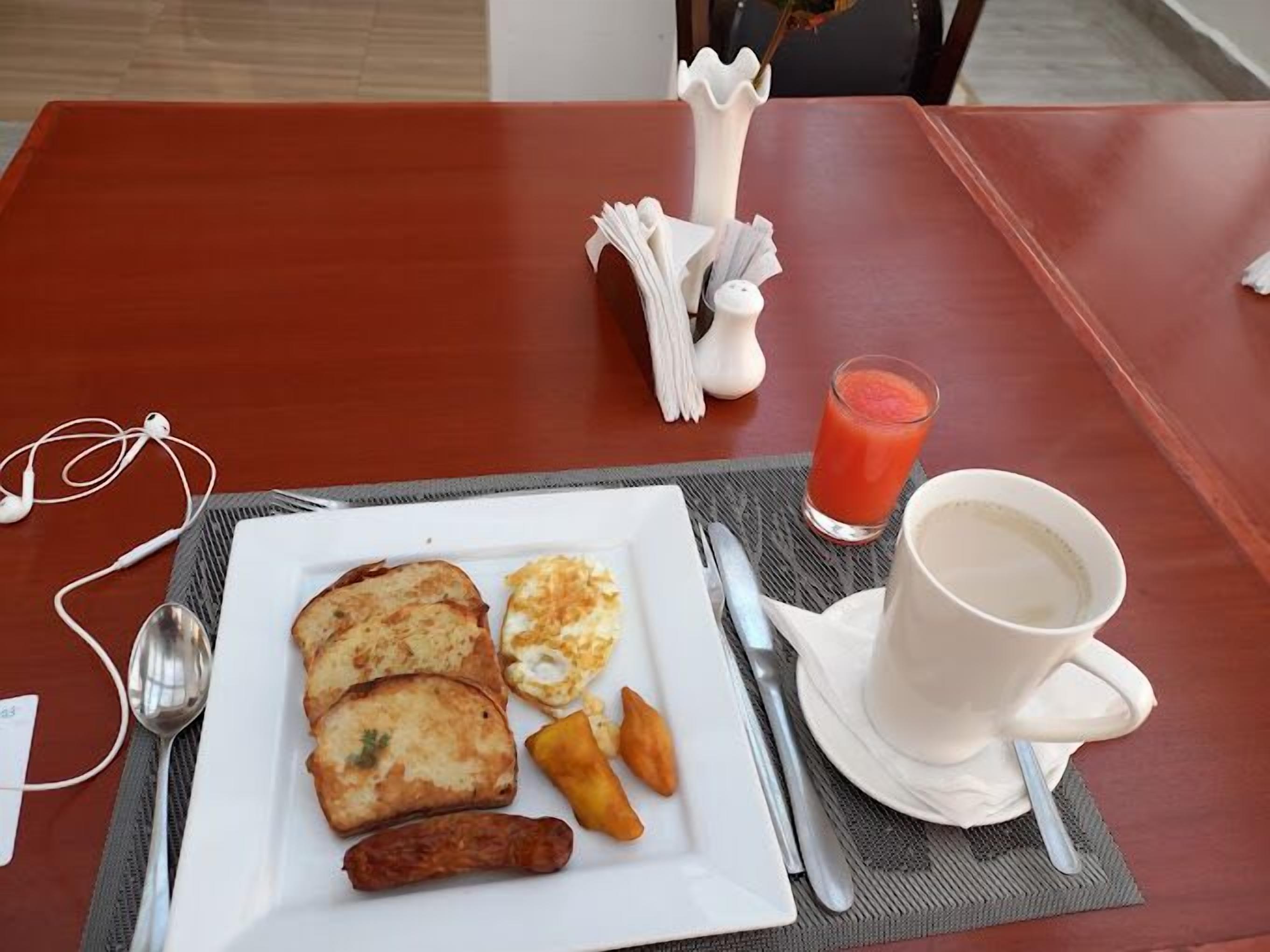 A breakfast plate with toast, eggs, sausage, and hash browns on a table with a cup of coffee and a glass of orange juice.