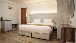 A bedroom with a large bed, a wooden wardrobe, a bedside table, and a mirror. - Grand Tiara Hotel Naivasha (Naivasha)