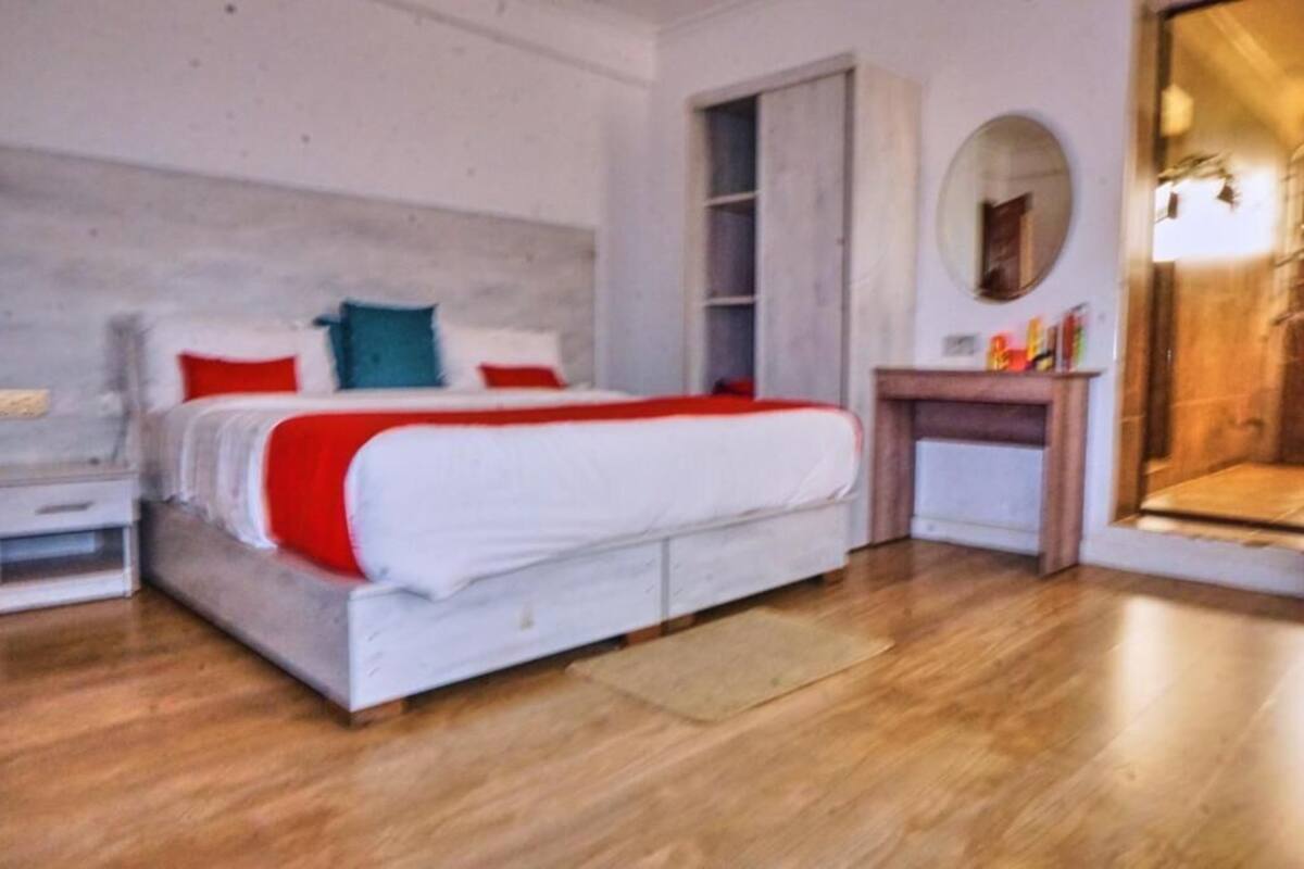 A bedroom with a bed, a nightstand, a dresser, a mirror, and a wooden floor.