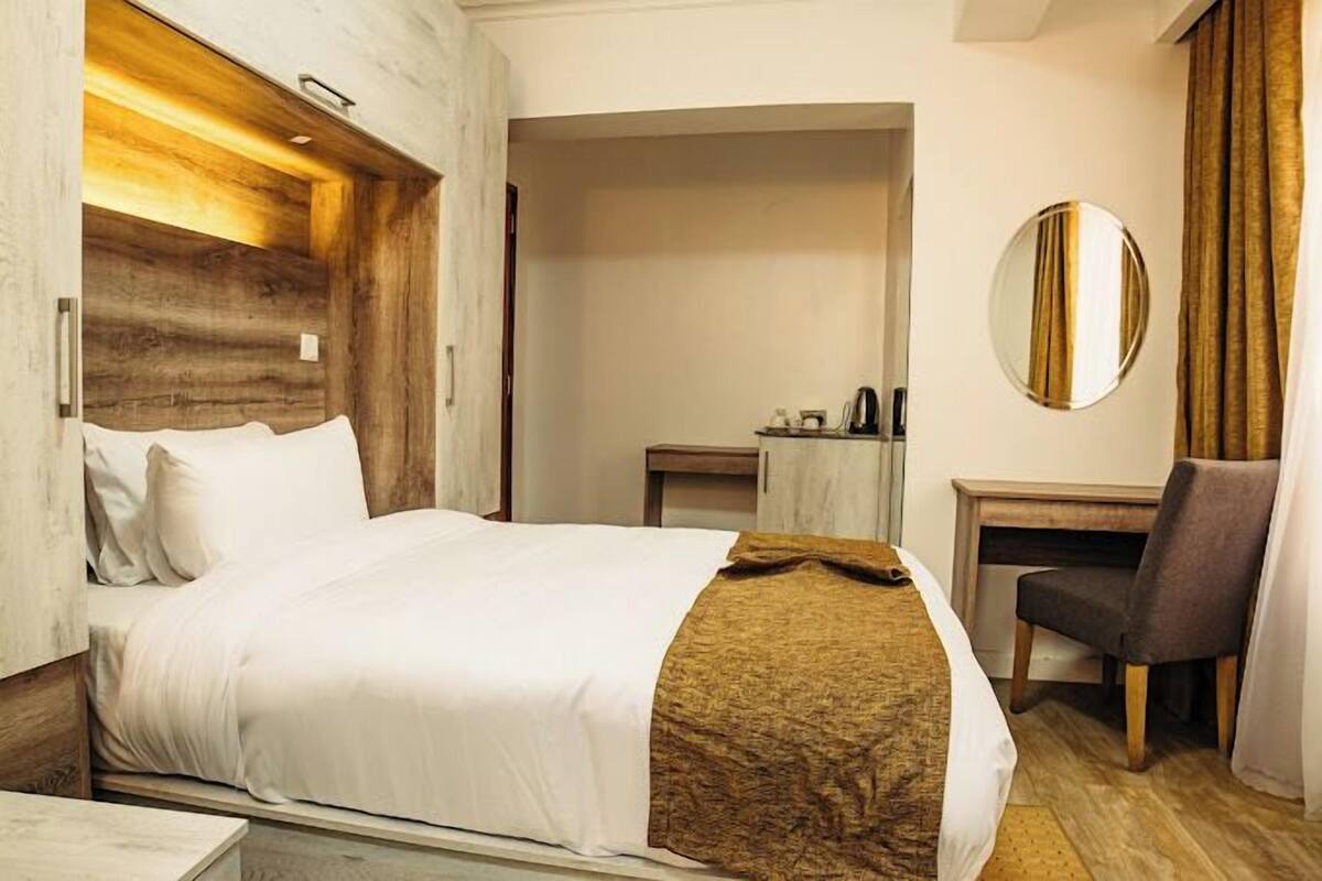 A hotel room with a bed, a desk, a chair, and a mirror.
