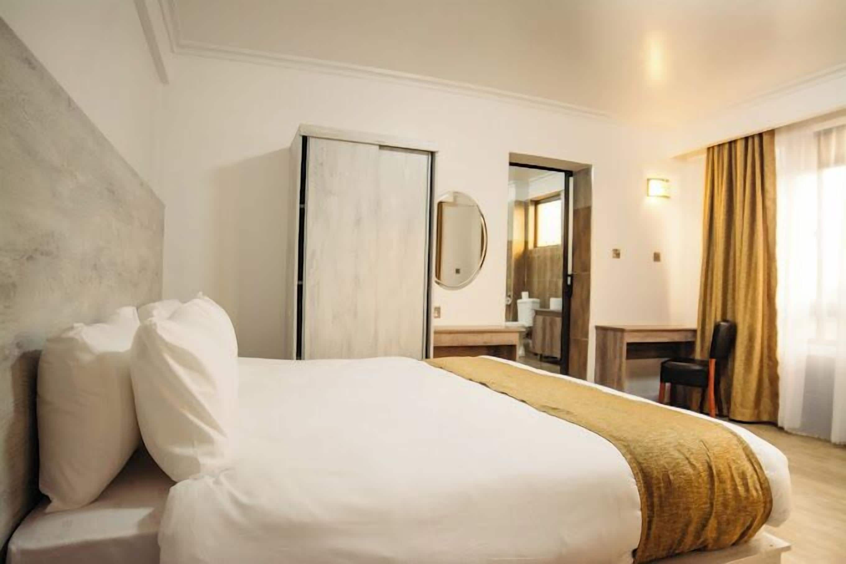 Ett hotellrum med en stor säng, ett skrivbord, en stol, en spegel och en garderob.