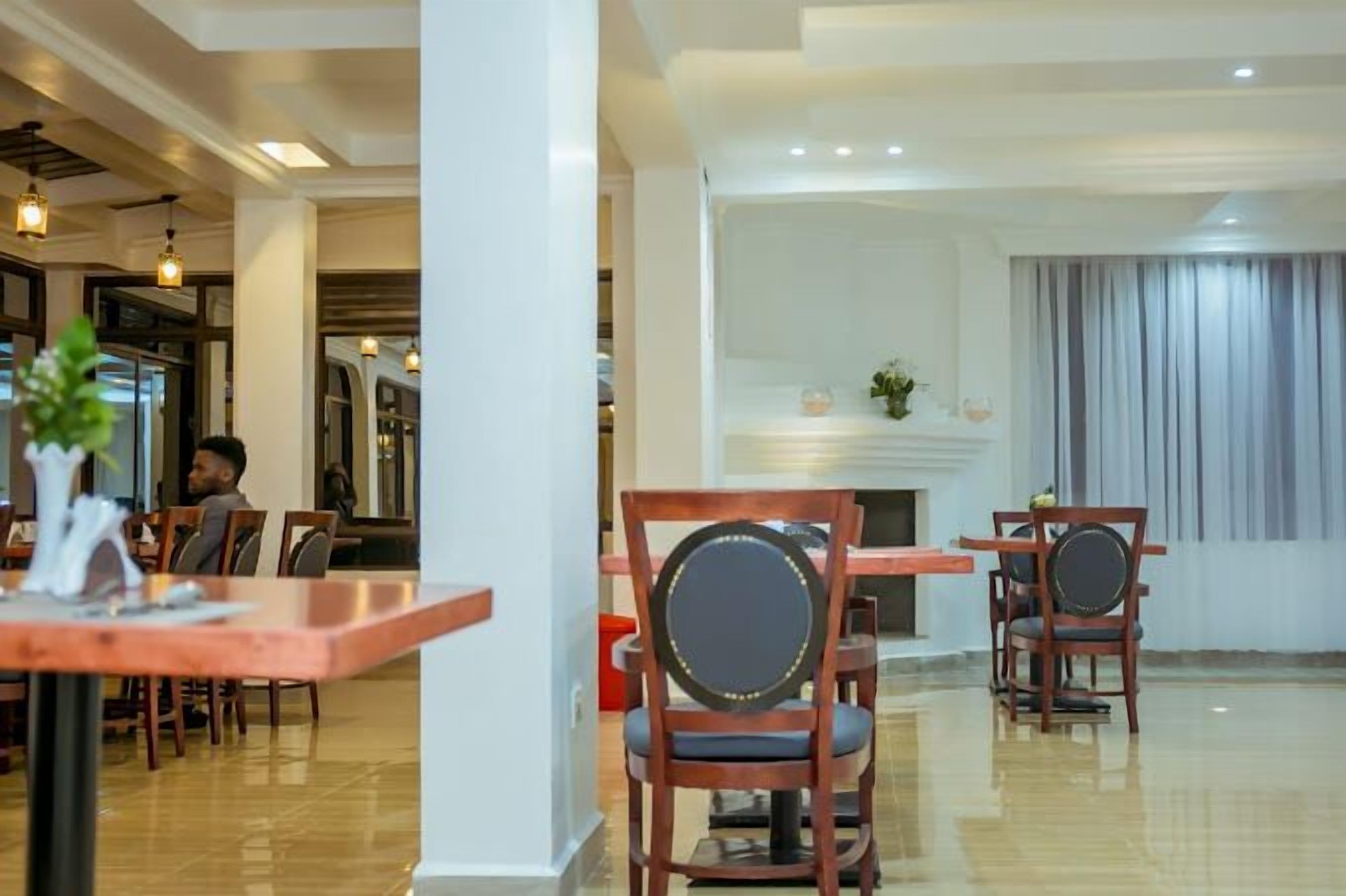 A hotel lobby with wooden tables and chairs, a fireplace, and a view of the dining area.