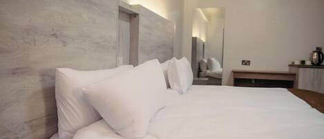 A hotel room with a large bed, a wooden headboard, and a small bedside table with a kettle.