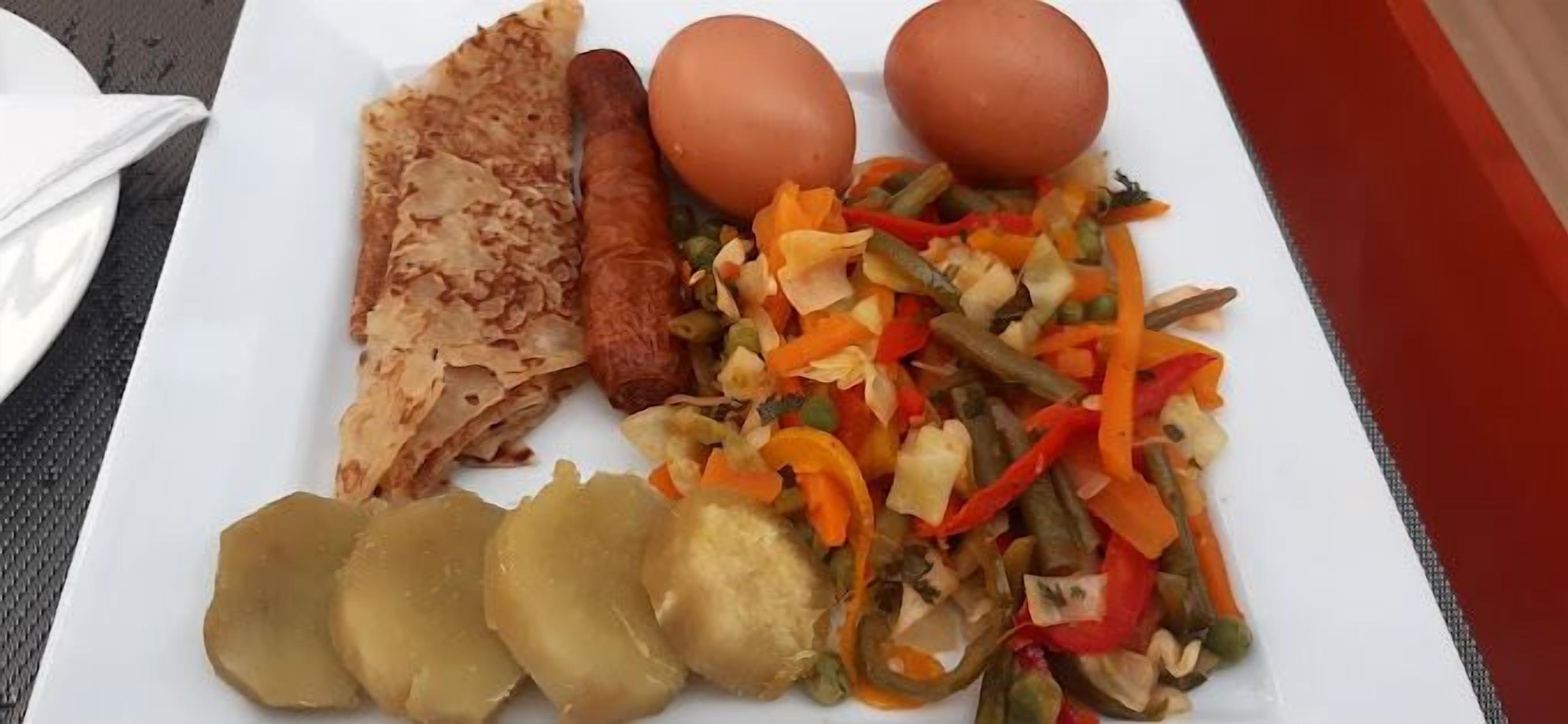 Une assiette comprenant une saucisse, deux œufs, une tranche de pain et un mélange de légumes.