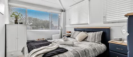 Une chambre moderne avec un grand lit, une armoire blanche et une fenêtre équipée de stores.