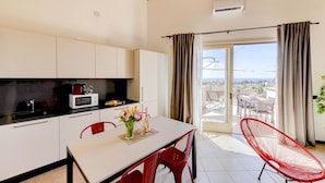 A modern kitchen with white cabinets, a dining table with red chairs, and a red chair by the window. - Palazzo Garda - Lakeview Penthouse 5 (Toscolano-Maderno)