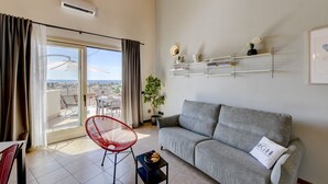 A living room with a grey sofa, a red chair, a small table with a bowl of fruit, and a balcony with a view. - Palazzo Garda - Lakeview Penthouse 5 (Toscolano-Maderno)