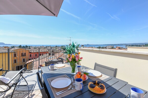 A table set outdoors with a view of the city, a vase with flowers, and a plate of food.