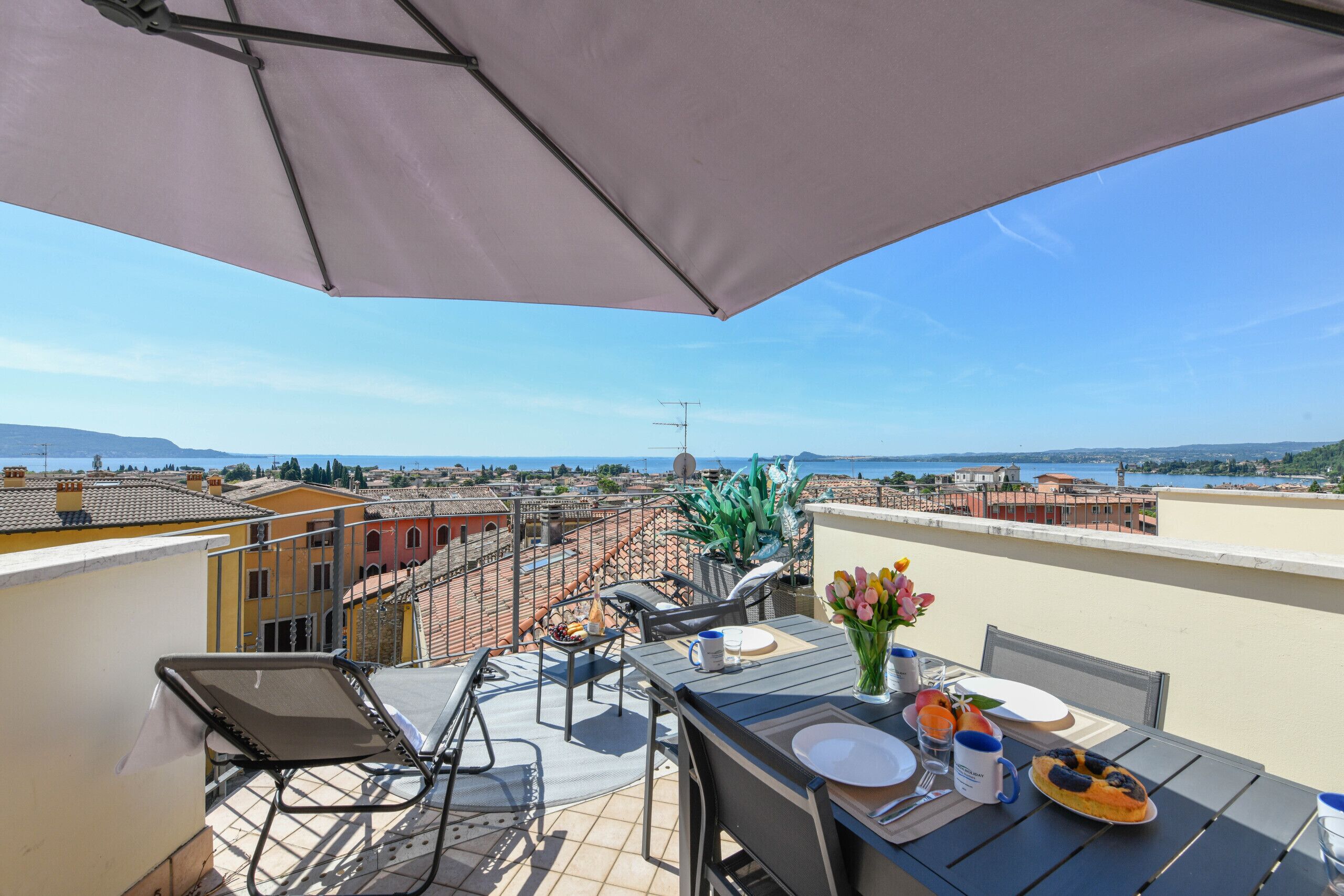 A rooftop terrace with a table set for two, a chair, and a view of the cityscape.