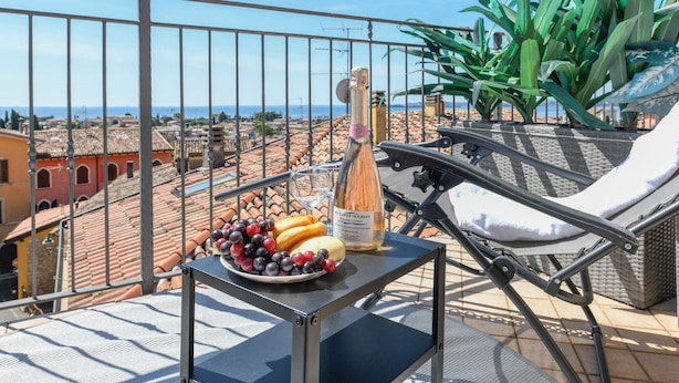 A balcony with a table, a bottle, and a plate of fruit. - Palazzo Garda - Lakeview Penthouse 5 (Toscolano-Maderno)