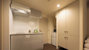 A compact kitchen with a built-in dishwasher, a microwave, and a small refrigerator. There are cabinets with a microwave on top and a sink with a faucet.