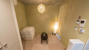 A hotel room with a bed, a small table with a plant, a lamp, a trash bin, and a wall-mounted phone.