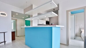A modern kitchen with a blue island, recessed lighting, and a view into the adjacent living area. - GuestHost - Vento di Mare House (Naples)